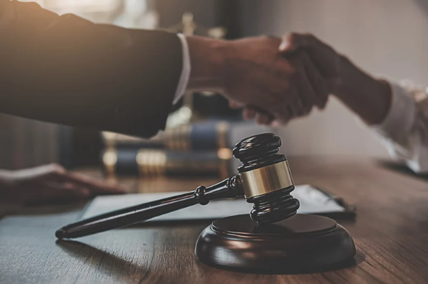 Closeup shot of hands shaking with a legal gavel in the foreground